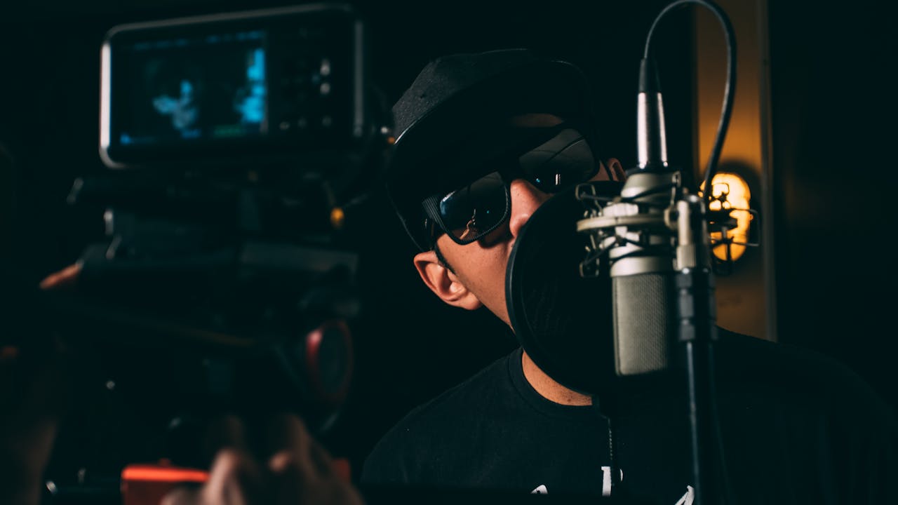 A hip-hop artist records vocals in a dark, atmospheric studio setting.